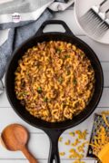 On the counter is a skillet of cheesy hamburger skillet, with a wooden spoon and other ingredients featured.