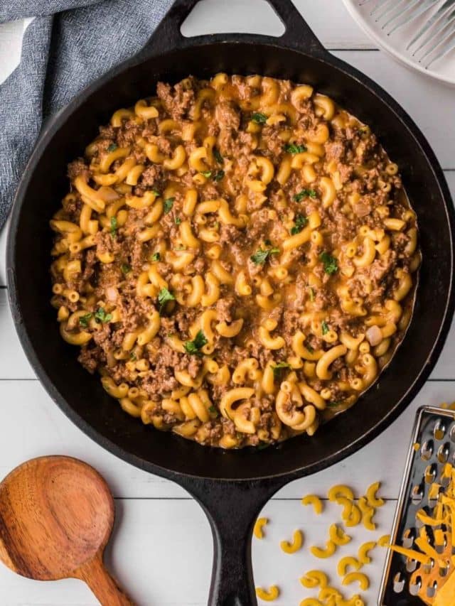 On the counter is a skillet of cheesy hamburger skillet, with a wooden spoon and other ingredients featured.