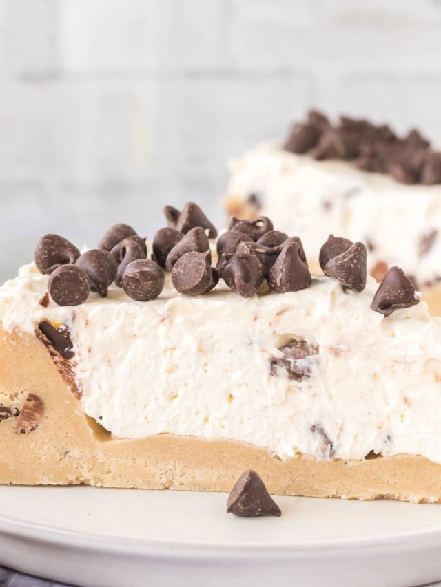 A slice of no-bake cookie dough cheesecake topped with chocolate chips on a white plate.
