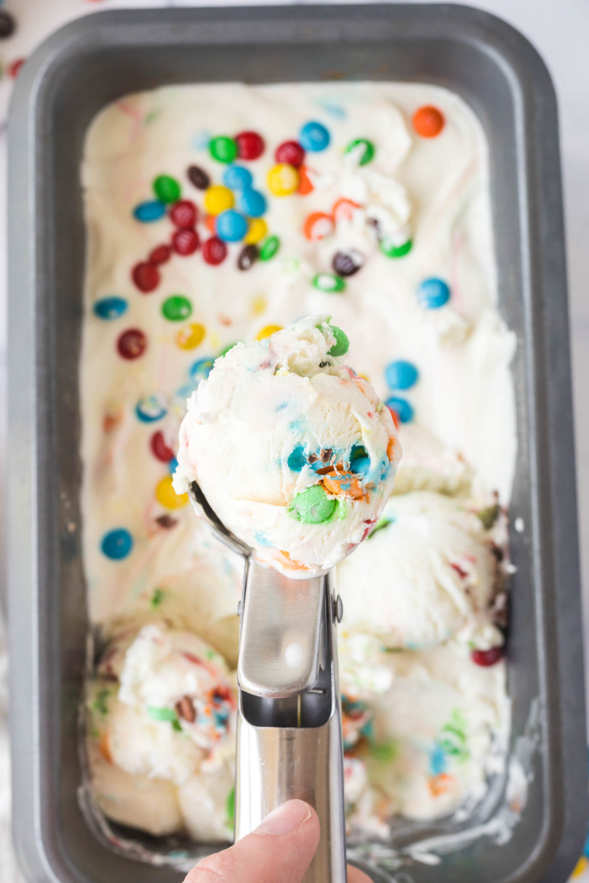 Removing a scoop of M&M Ice Cream with an ice cream scoop from a pan.