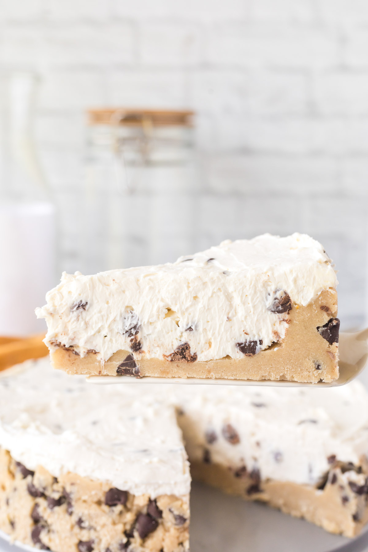 A slice of chocolate chip cookie dough cheesecake being removed from the whole no-bake cheesecake.