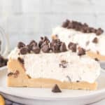 A slice of no-bake cookie dough cheesecake topped with chocolate chips on a white plate.