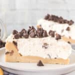 A slice of no-bake cookie dough cheesecake topped with chocolate chips on a white plate.