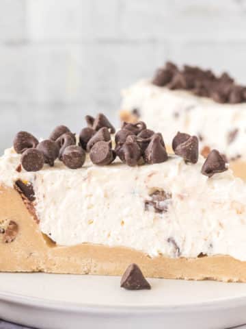 A slice of no-bake cookie dough cheesecake topped with chocolate chips on a white plate.