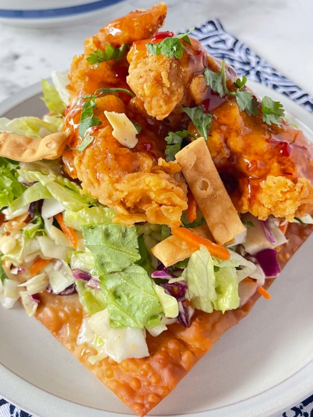 Asian Crunch Chicken Salad on a egg roll wrapper base set on a white plate on top of a blue and white placemat.