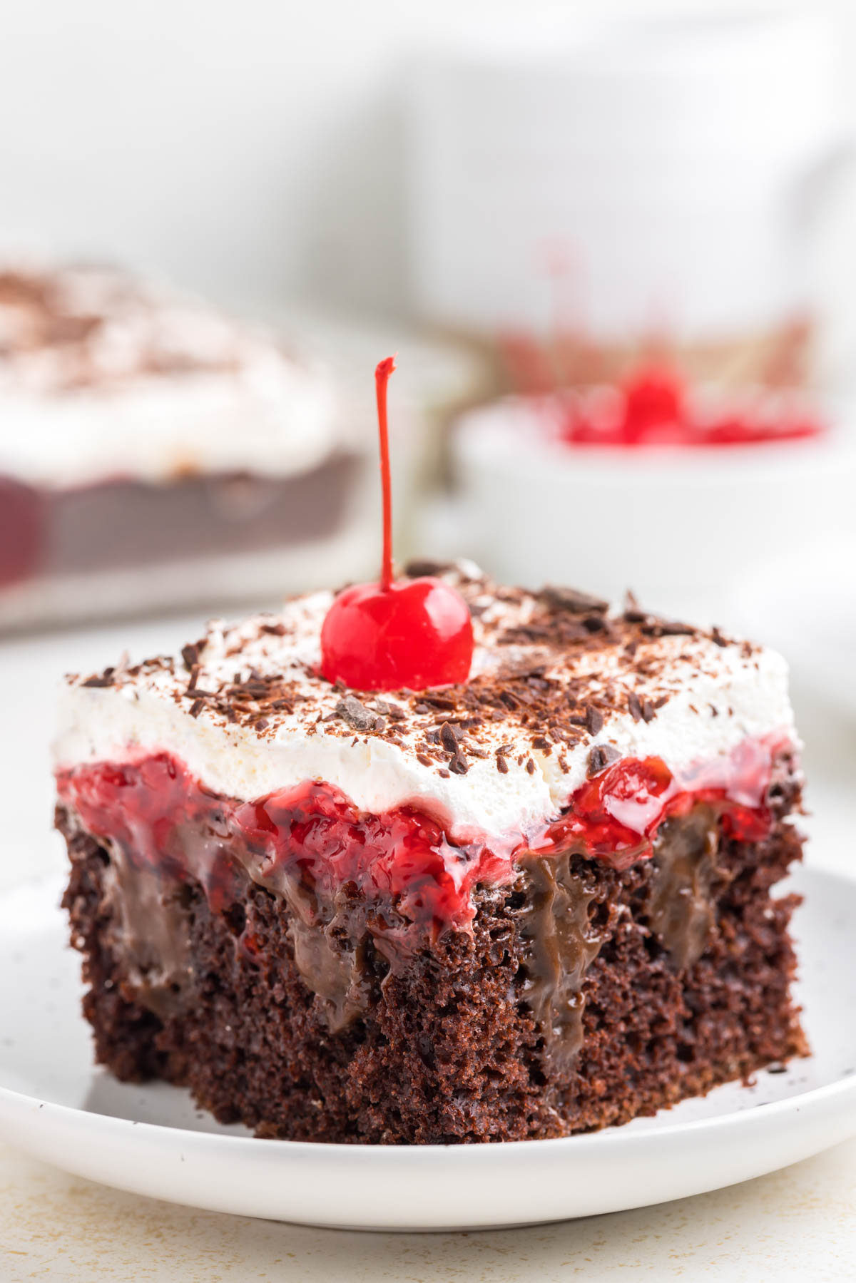 A slice of black forest poke cake topped with a cherry.