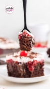A fork holds a bite of the black forest poke cake with a serving in the background.