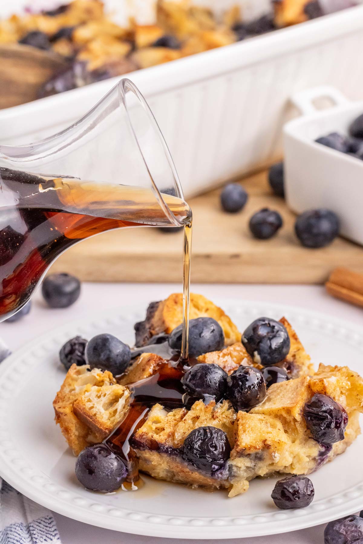 Syrup being poured over a plate of blueberry french toast casserole.