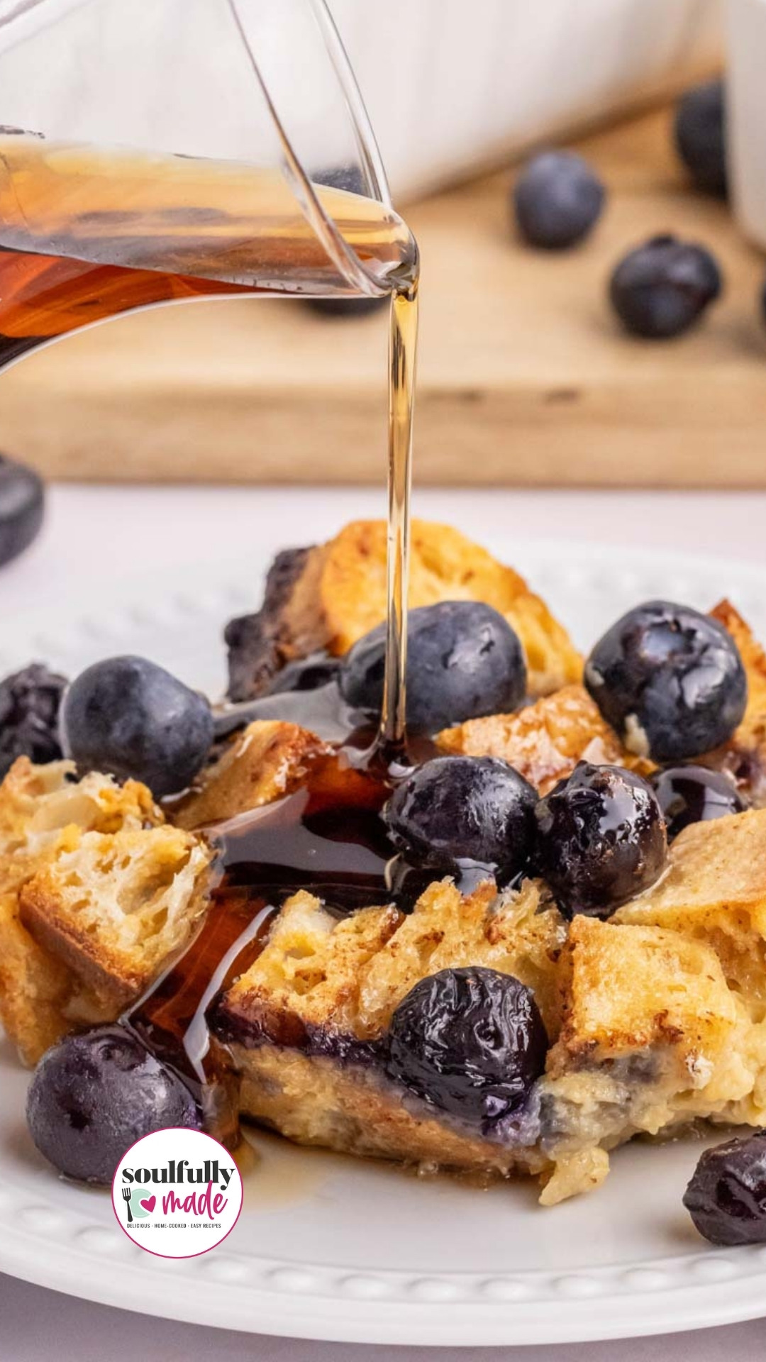 A Pinterest image of syrup being poured over a plate of blueberry french toast casserole.