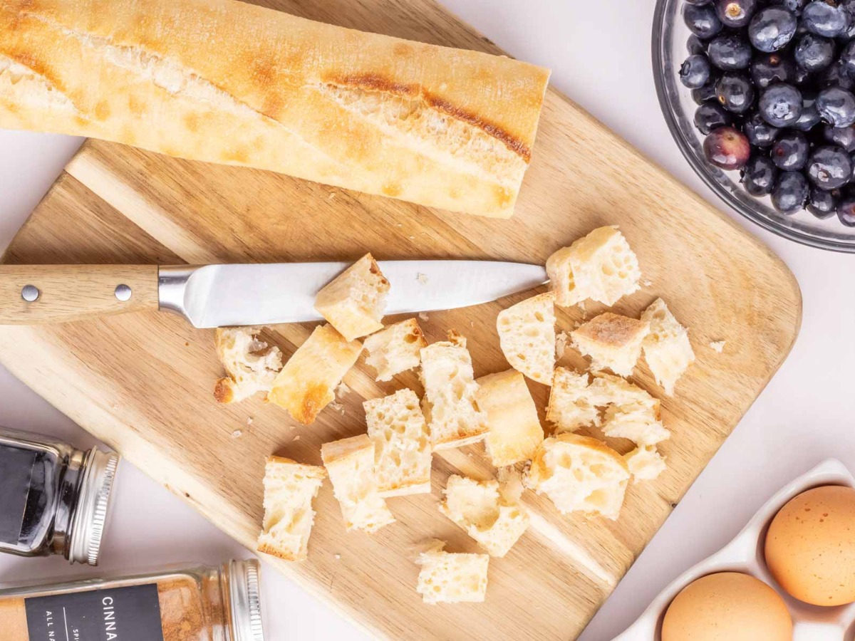 A french loaf sliced into cubes on a wooden cutting board.