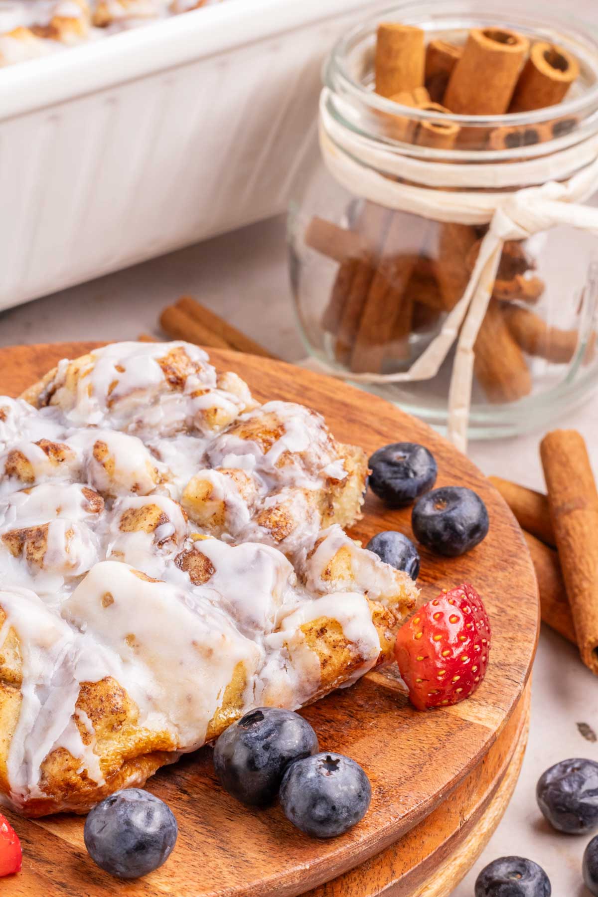 A wooden plate with a scoop of the casserole garnished with blueberries and strawberries.