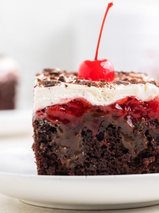 A square serving of Black Forest Poke Cake reveals the moist layers and it is topped with shaved chocolate and a red cherry.