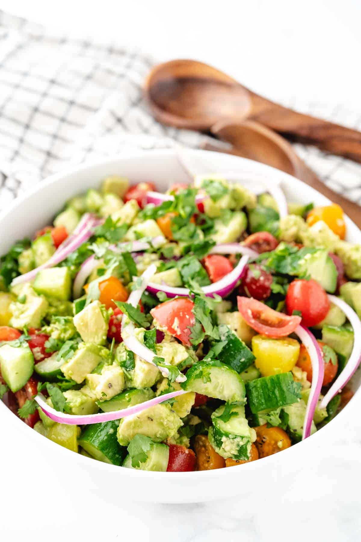 A close up of a bowl of cucumber tomato avocado salad after tossed and placed in a white serving bowl.