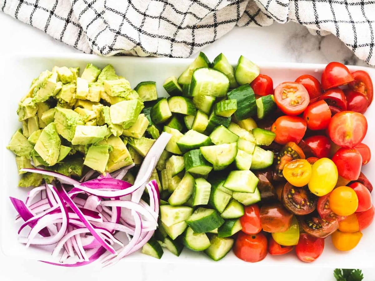 A tray of cut veggies - tomatoes, cucumber, avocado, and sliced red onion.