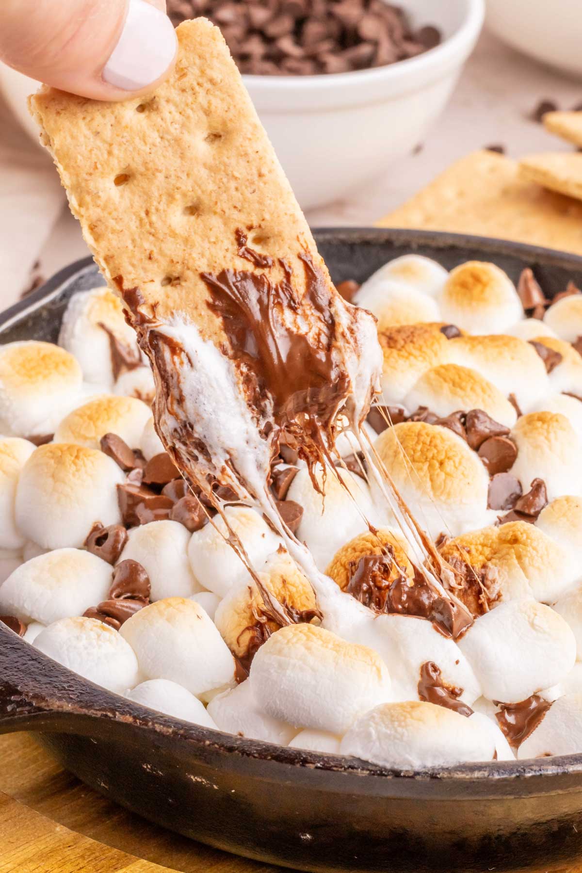 Removing gooey s'mores dip with a honey graham cracker.