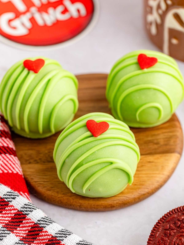Three Grinch Christmas truffles on a wooden plate.