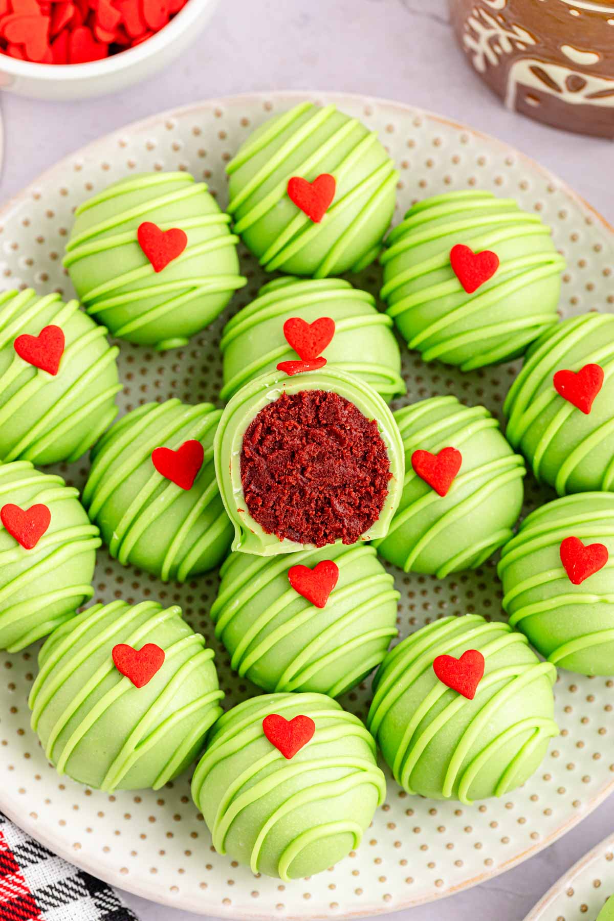 A serving plate of Grinch Oreo Balls with one cut open showing the red velvet oreo center.