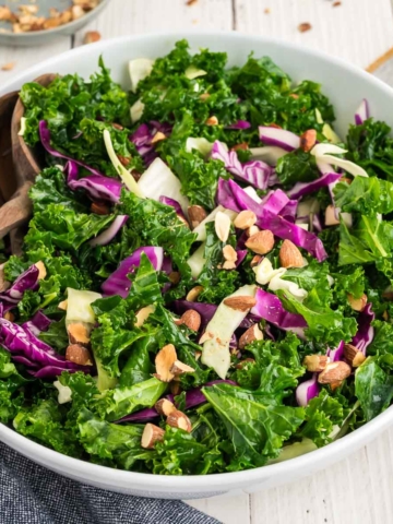 A kale crunch salad in a white bowl topped with toasted almonds.