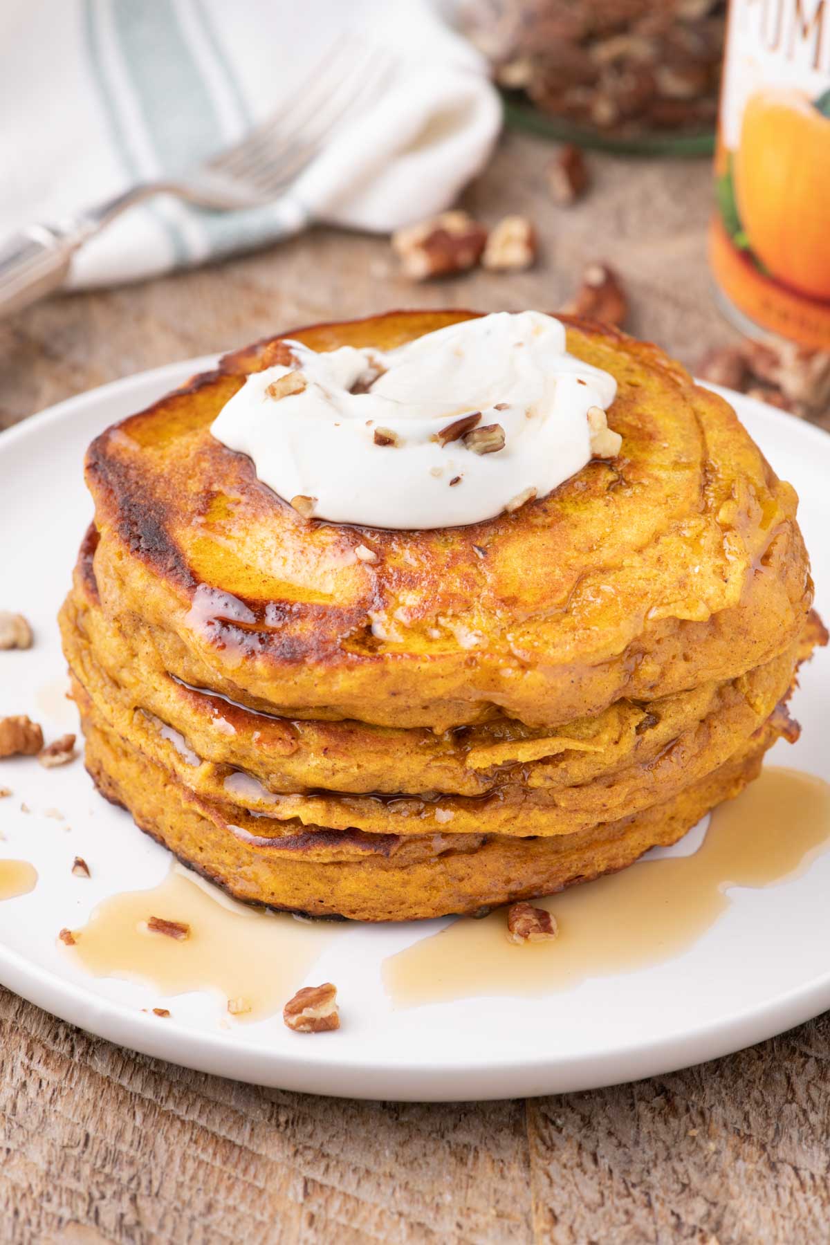 A stack of pumpkin pancakes on a white plate set on a wooden table.