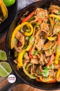 A close up overhead shot of the cast-iron skillet full of the steak, peppers, and onions for steak fajitas.