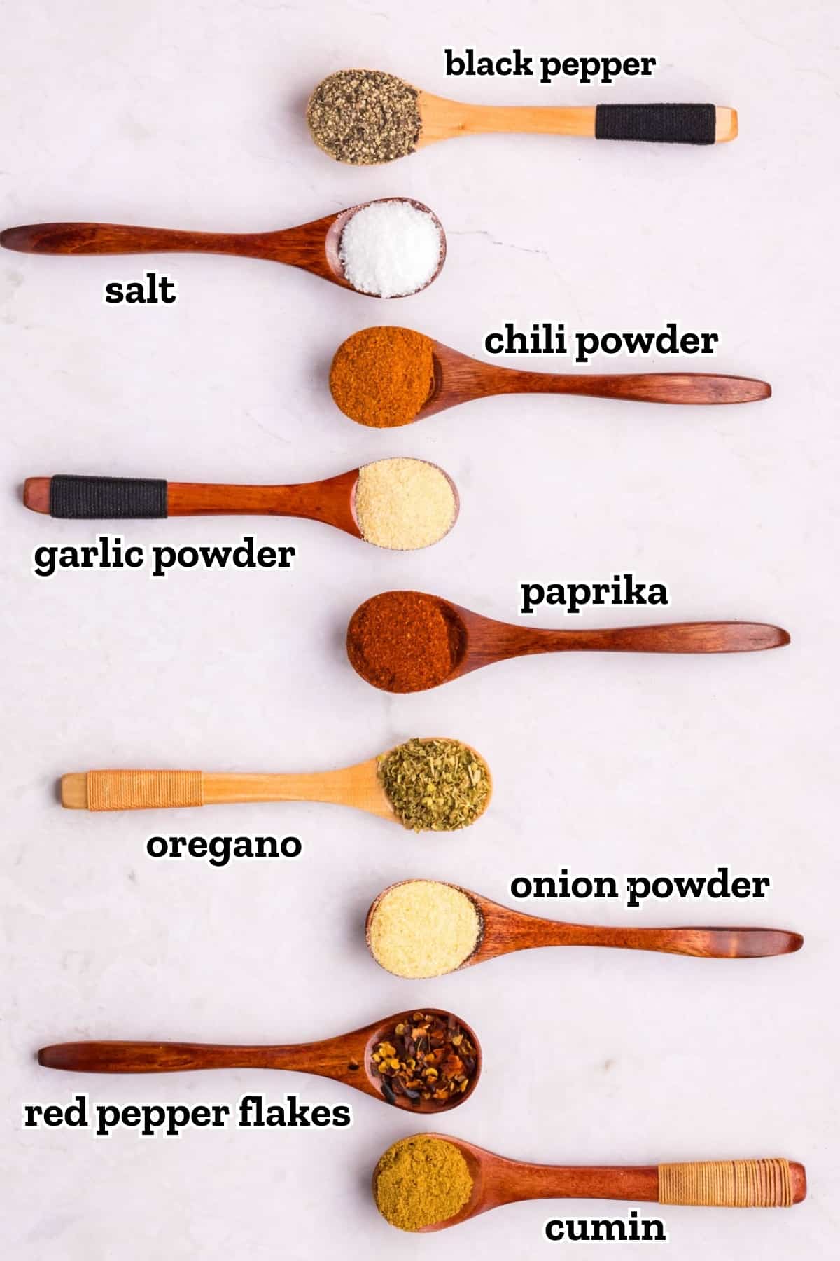 Measuring spoons laid out on a table labeled with each spice needed to make homemade taco seasoning.