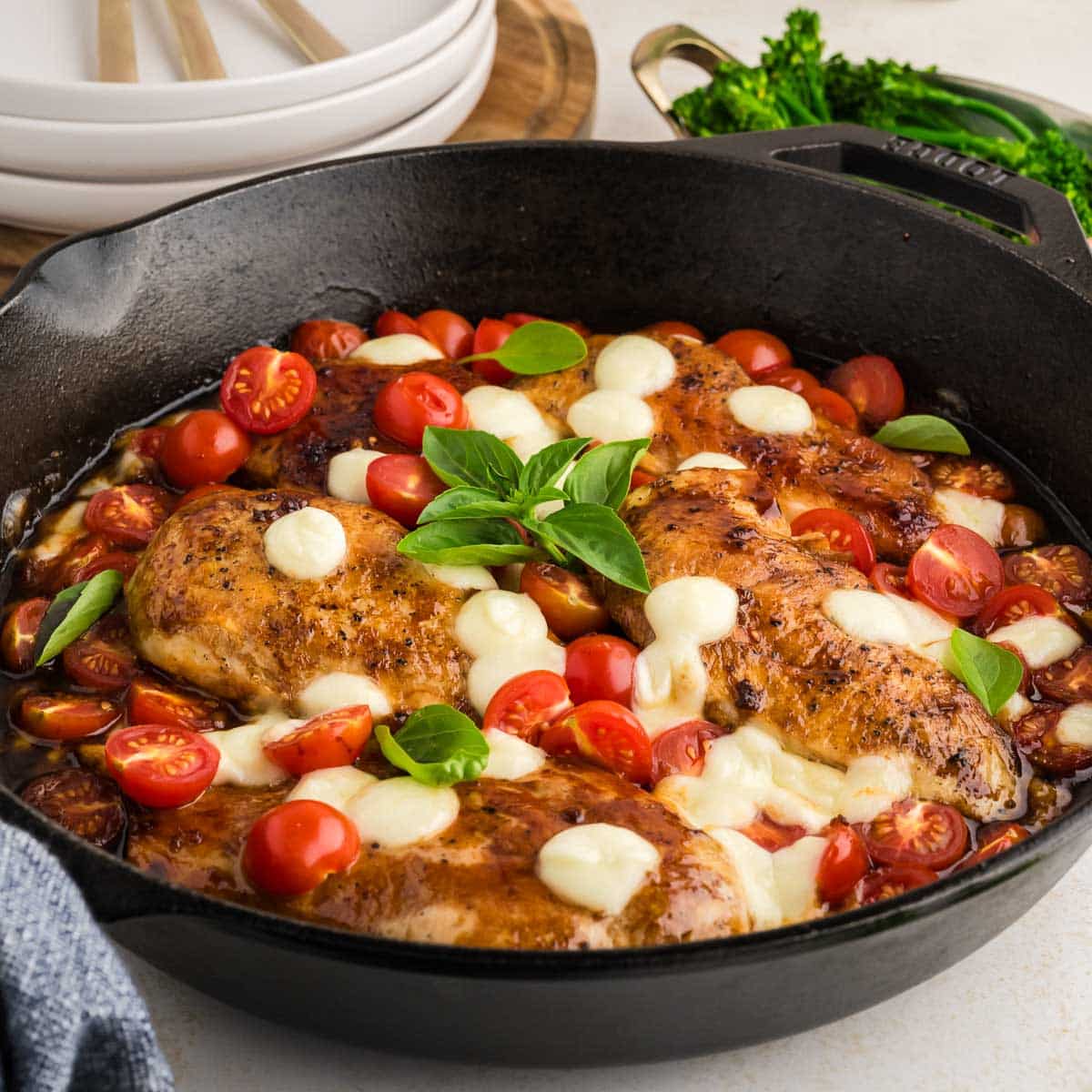 A cast iron skillet filled with balsamic chicken with tomatoes and mozzarella cheese.