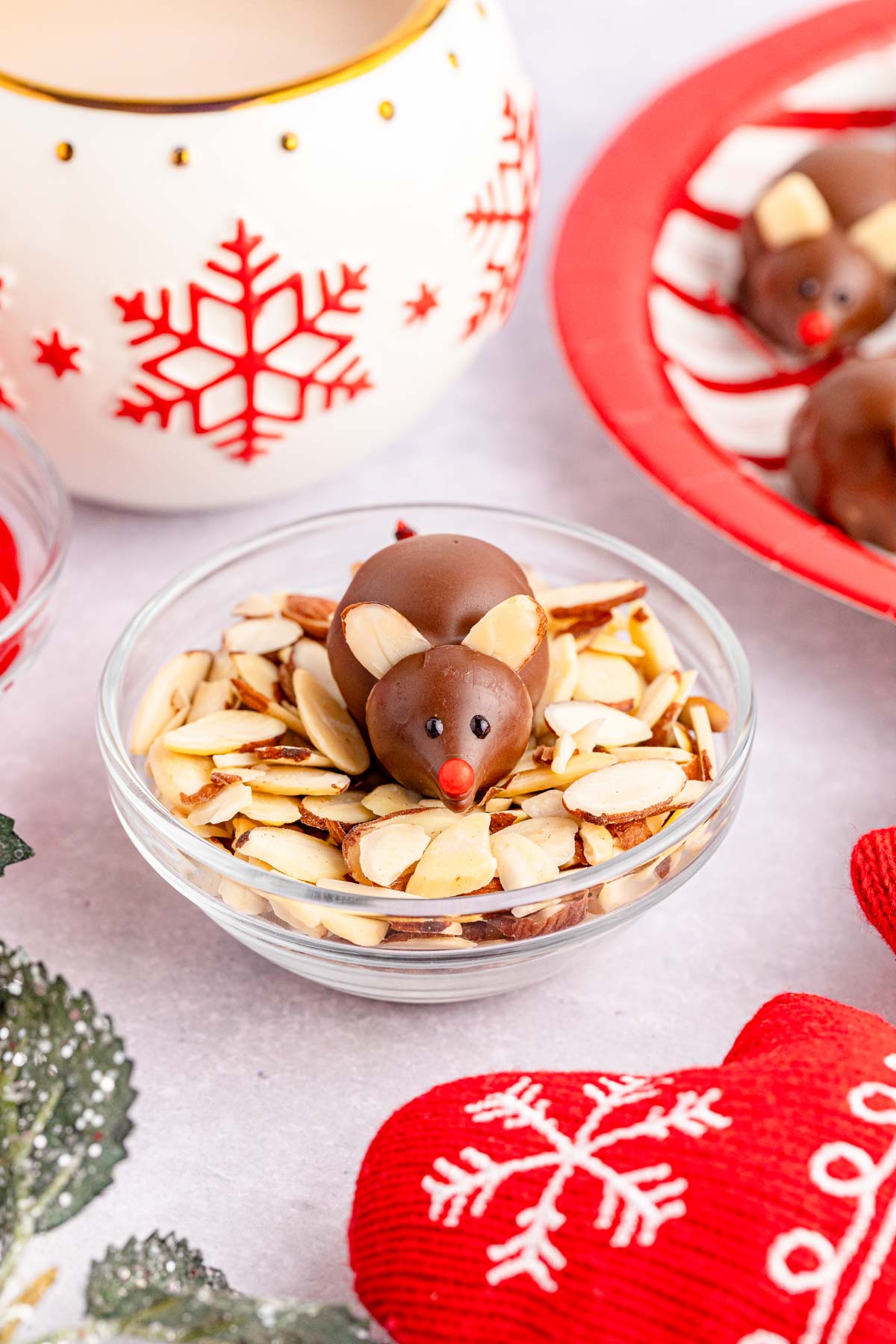 Chocolate covered candy mice set in a bowl of sliced almonds on a Christmas tablescape.