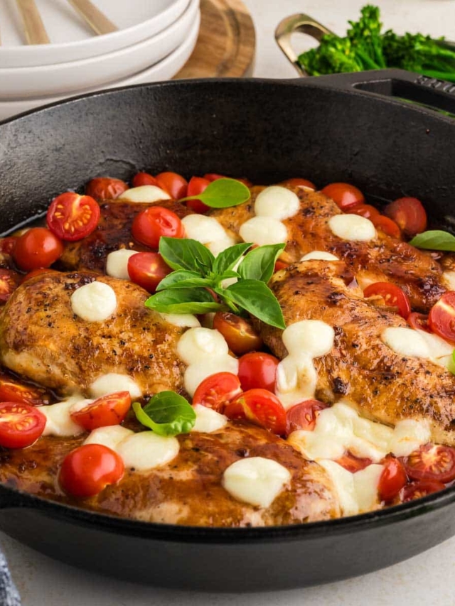 A cast iron skillet filled with balsamic chicken with tomatoes and mozzarella cheese.