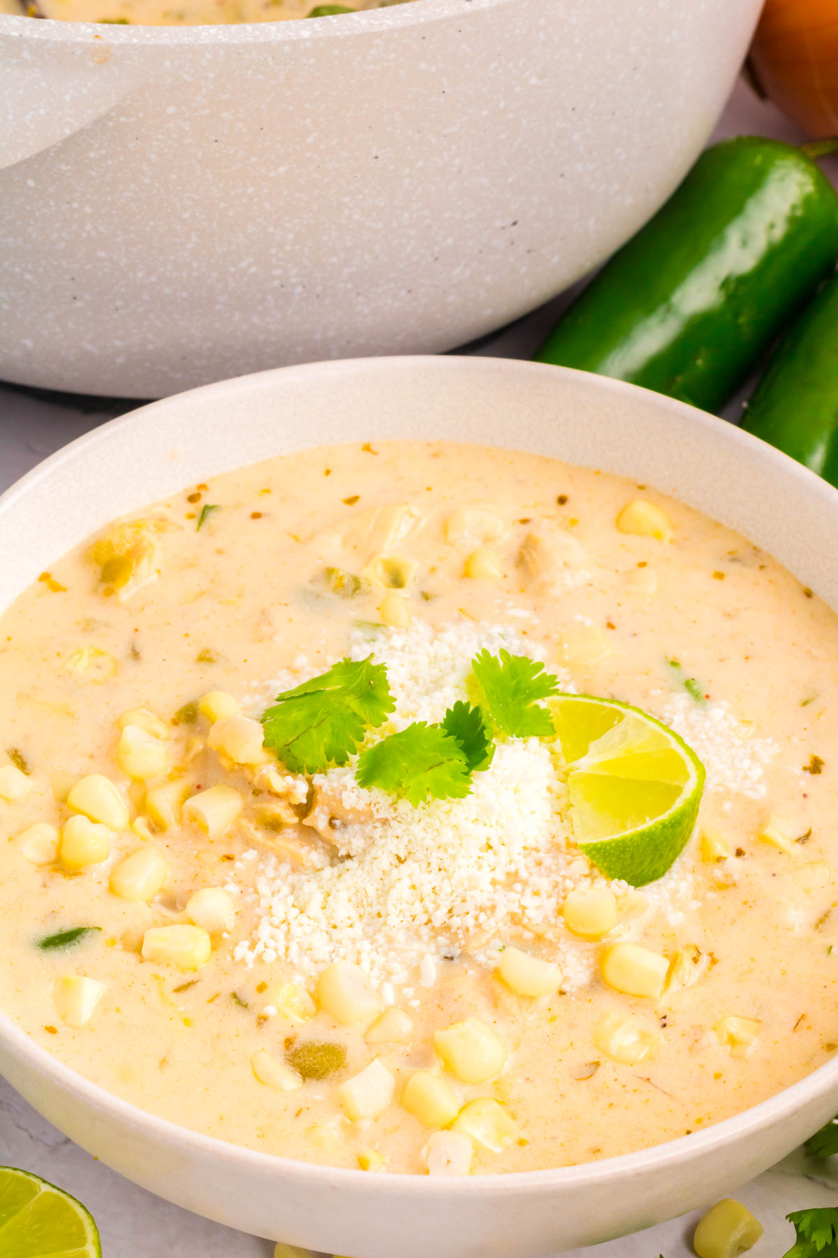 A bowl of street corn chili topped with corn kernels, Cotija cheese, cilantro and a lime wedge.