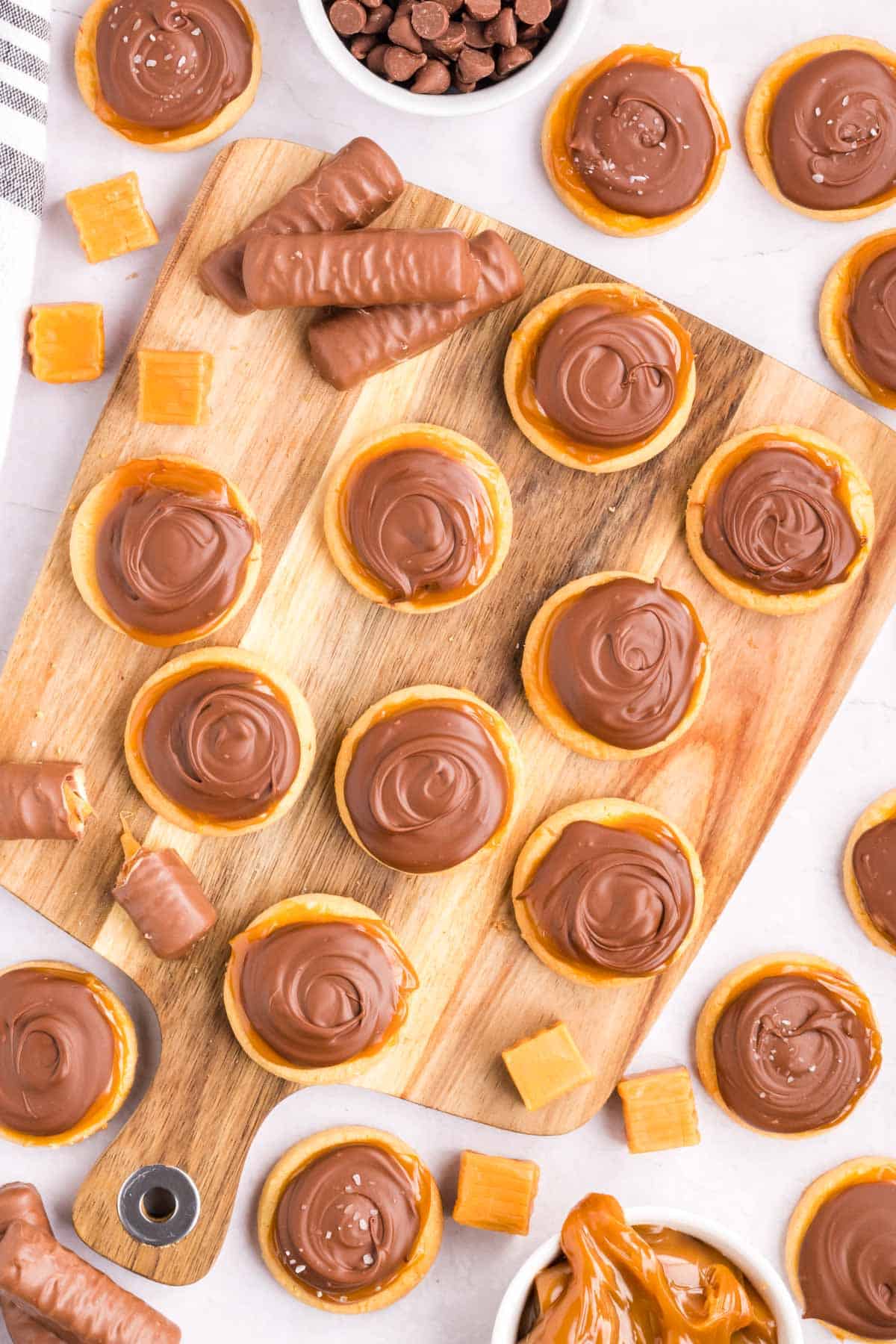 A wooden serving board filled with Twix Cookies and garnished with Twix candy bars and caramel squares.