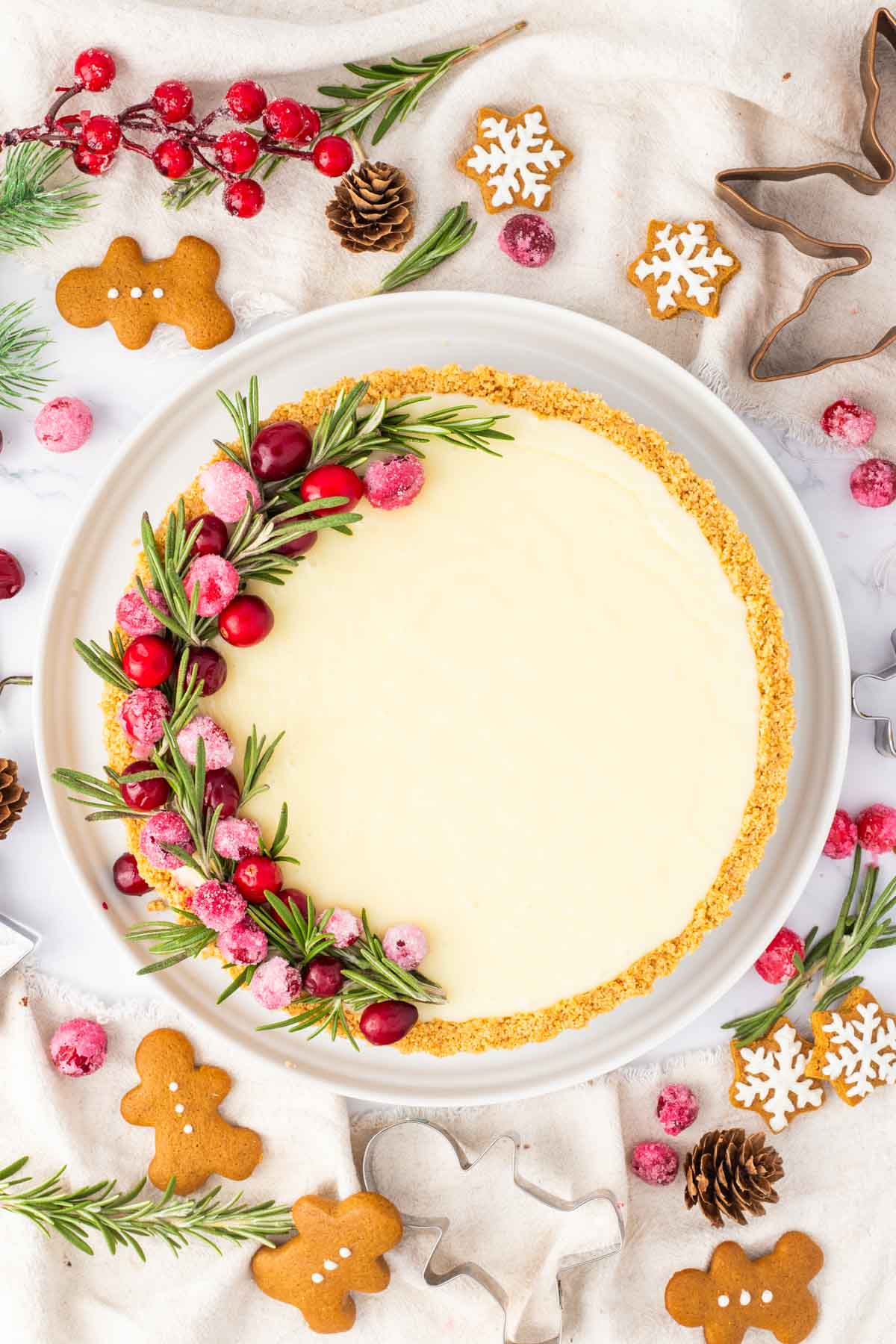A white chocolate tart garnished with sugared cranberries set on a tablescape with gingerbread men.