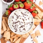 Easy Cannoli Dip in a white bowl served on a wooden serving board with broken waffle cones and strawberries.