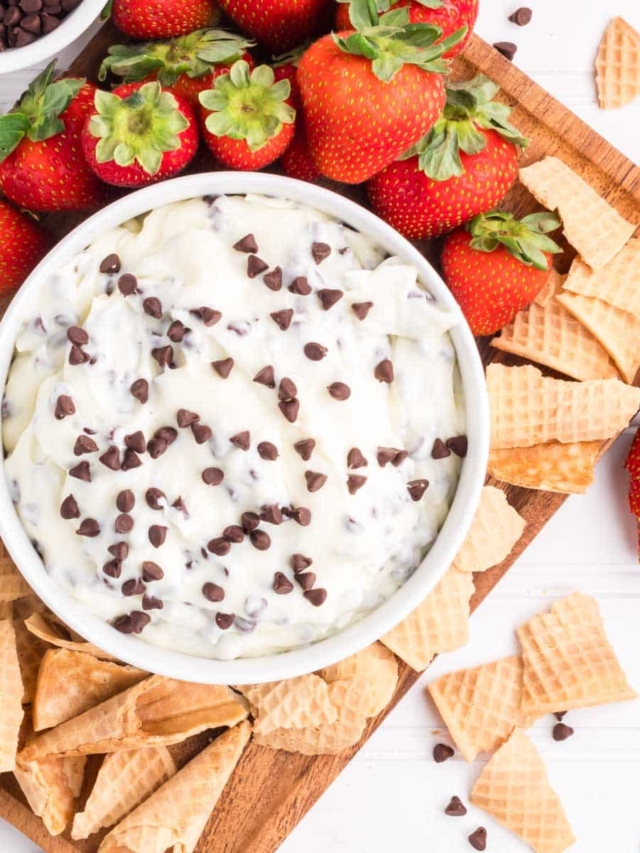 Easy Cannoli Dip in a white bowl served on a wooden serving board with broken waffle cones and strawberries.