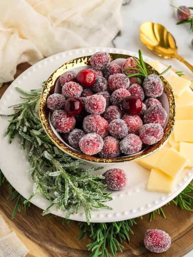 White bowl filled with sugared cranberries and garnished with sugared rosemary.