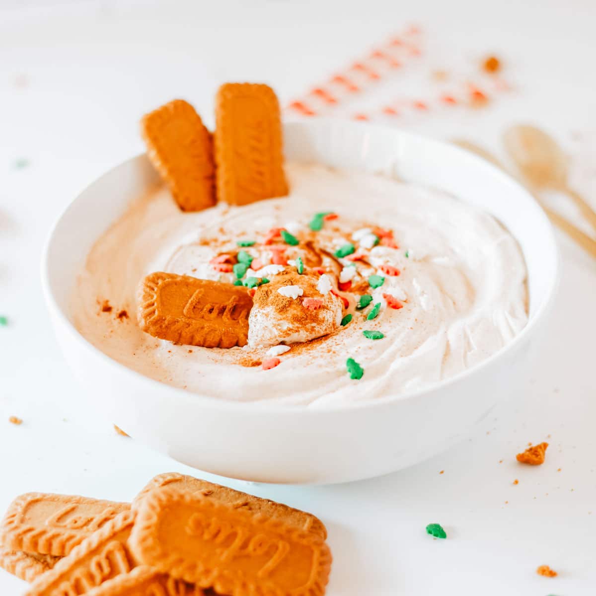 A white bowl filled with creamy eggnog dip garnished with cinnamon, Biscoff cookies, and spinkles.