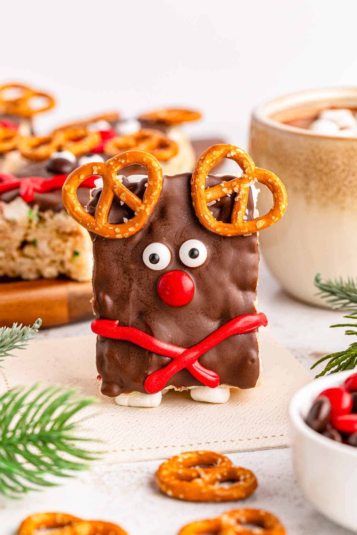 A reindeer rice krispies treat standing up with Christmas decor in the background.