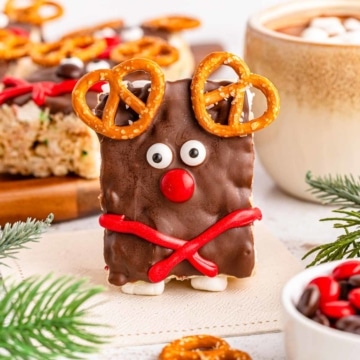 A reindeer rice krispies treat standing up with Christmas decor in the background.