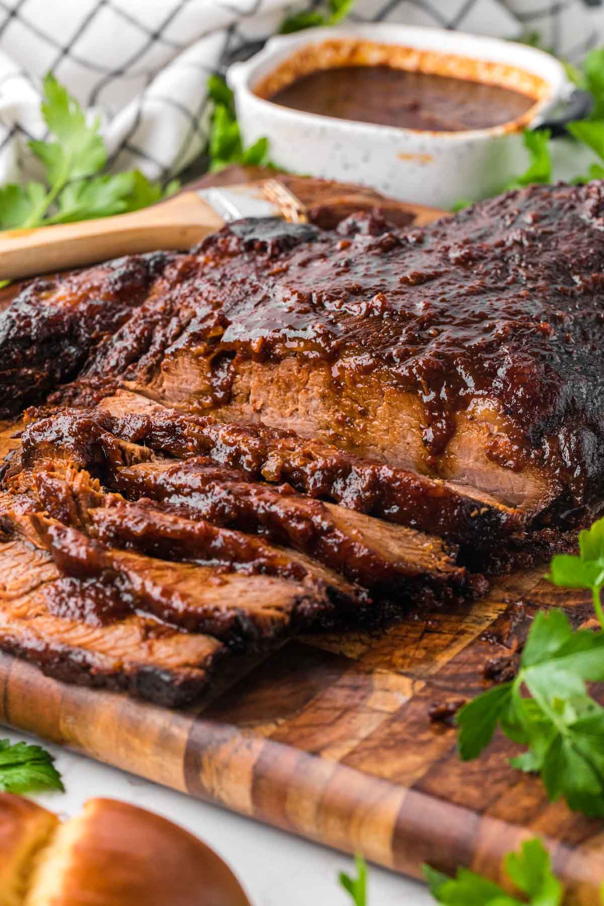 A beef brisket brushed with homemade bbq sauce on a wooden board garnish with parsley.