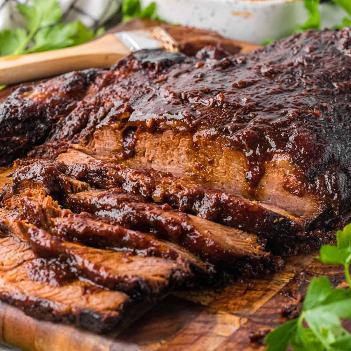 A beef brisket brushed with homemade bbq sauce on a wooden board garnish with parsley.