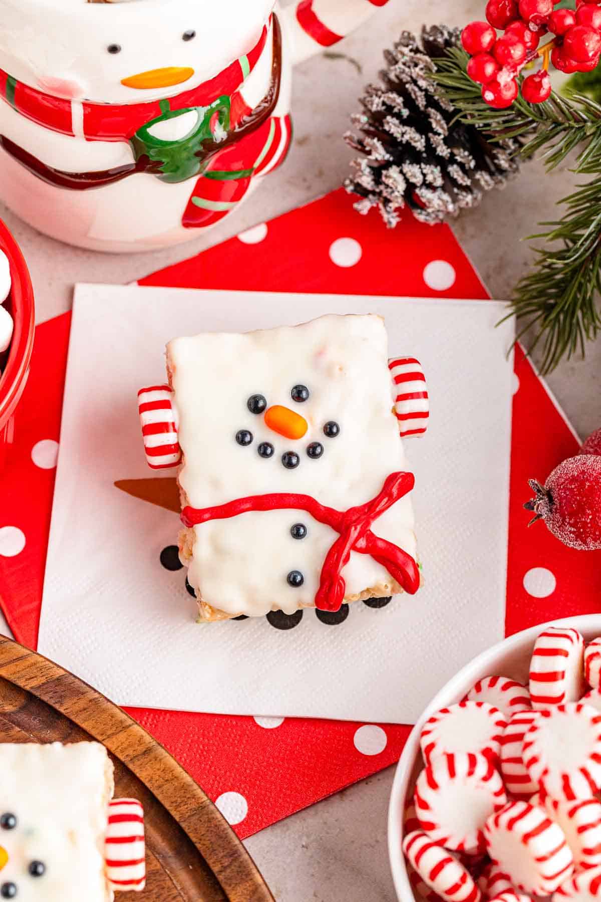 A cute snowman rice krispie treat decorated with black pearl candies, a tick tac nose, and peppermint ear muffs.