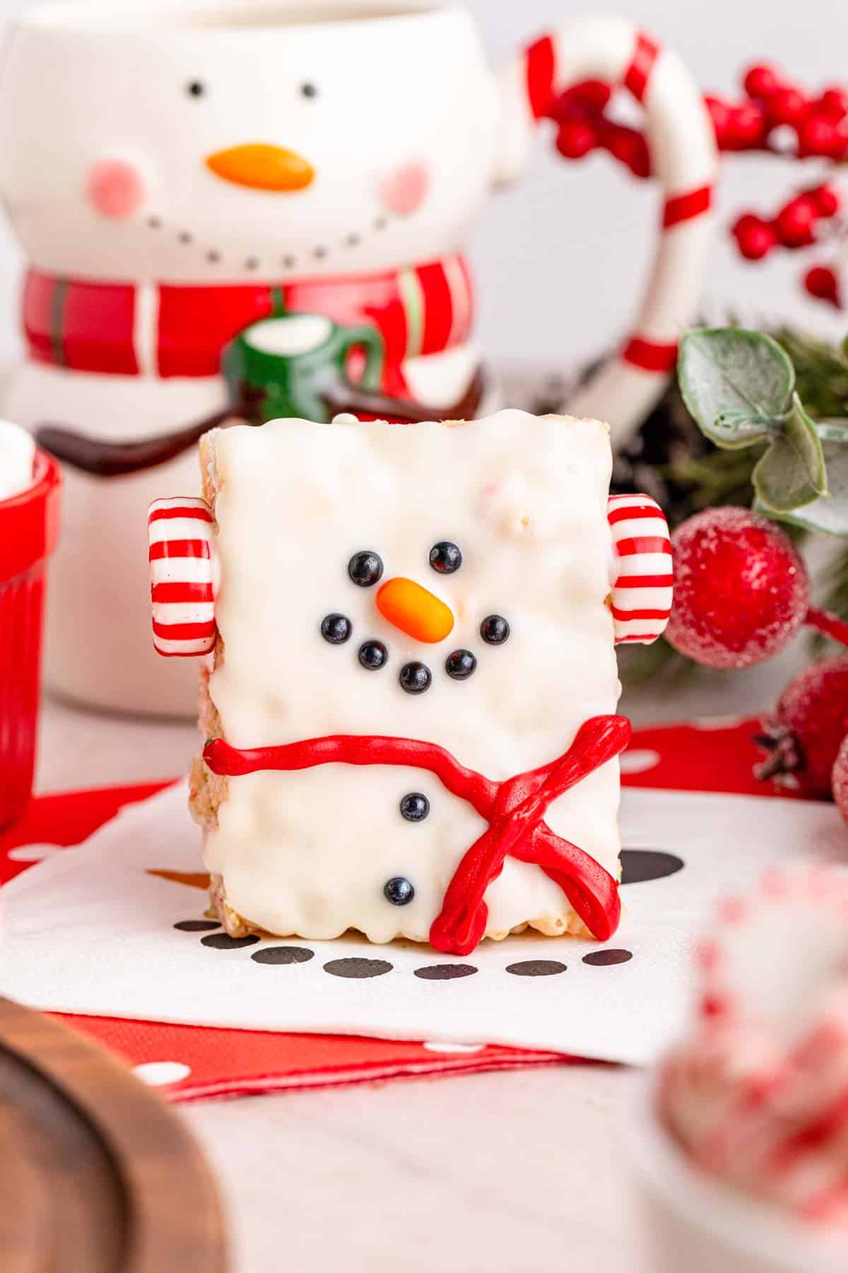 A snowman rice krispies treat standing up with Christmas decor in the background.