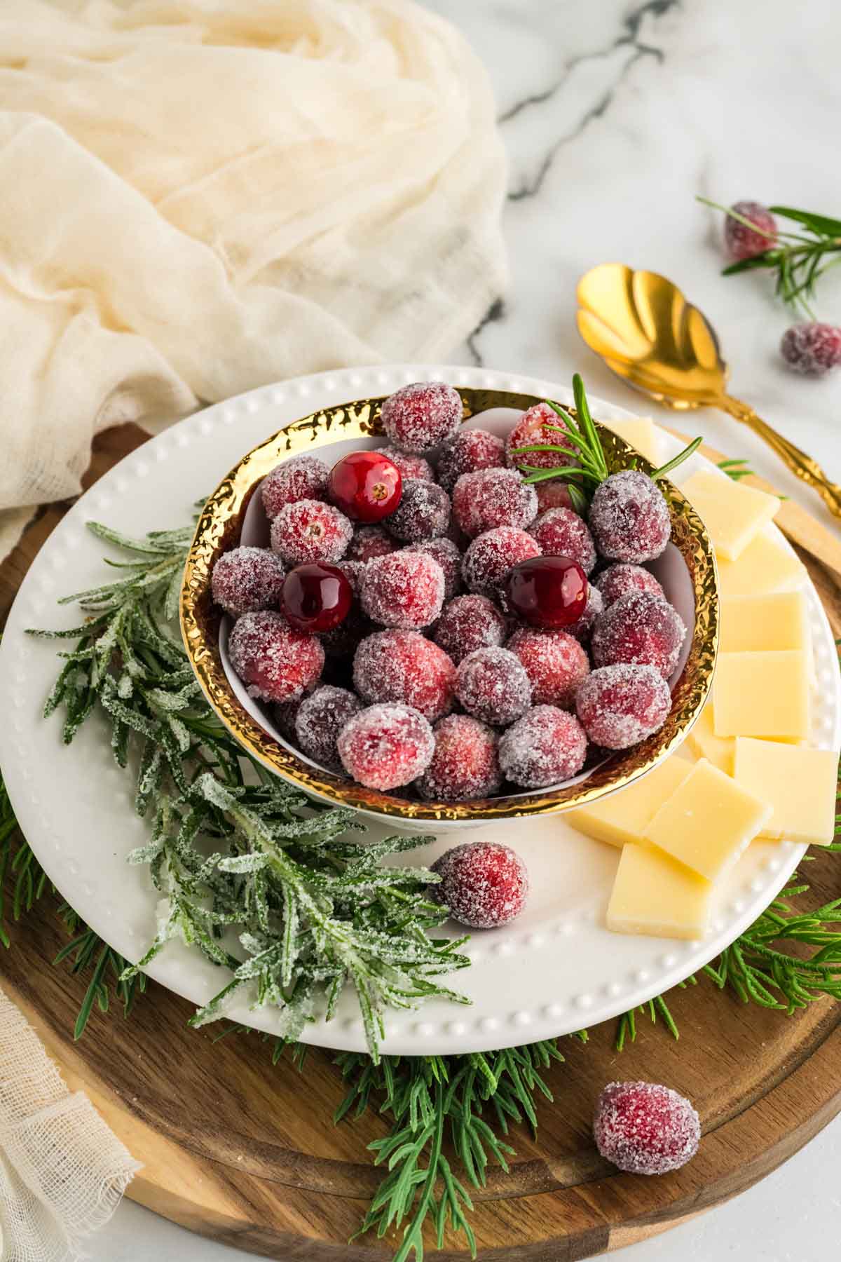 Homemade sugared cranberries served in a gold rimmed bowl with sliced white cheddar cheese.