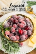 White plate with a gold rimmed bowl holding the sugared carnberries garnished with rosemary and cheese squares.