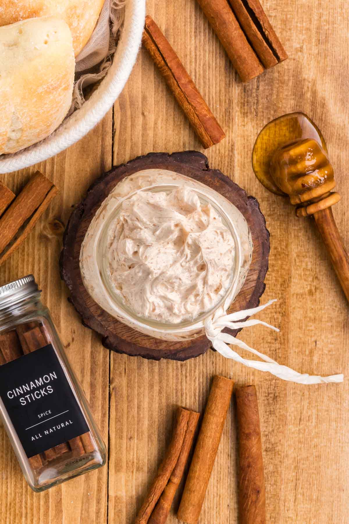 A wooden table set with rolls, whipped cinnamon butter, with cinnamon sticks and a honey served.