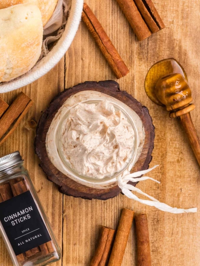 A wooden table set with rolls, whipped cinnamon butter, with cinnamon sticks and a honey served.