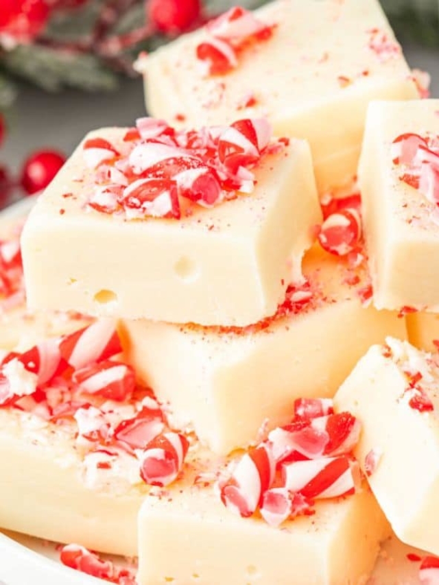 Peppermint vanilla fudge stacked on a plate and topped with crushed candy cane.