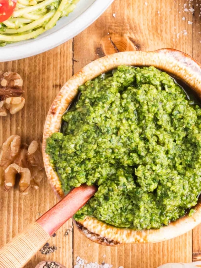 Blassic basil pesto in a bowl with a wooden spoon set on a wooden table.