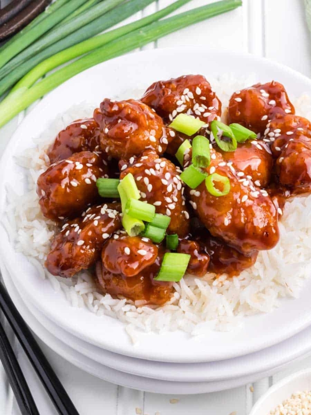Black chopsticks picking up Chinese sesame chicken.