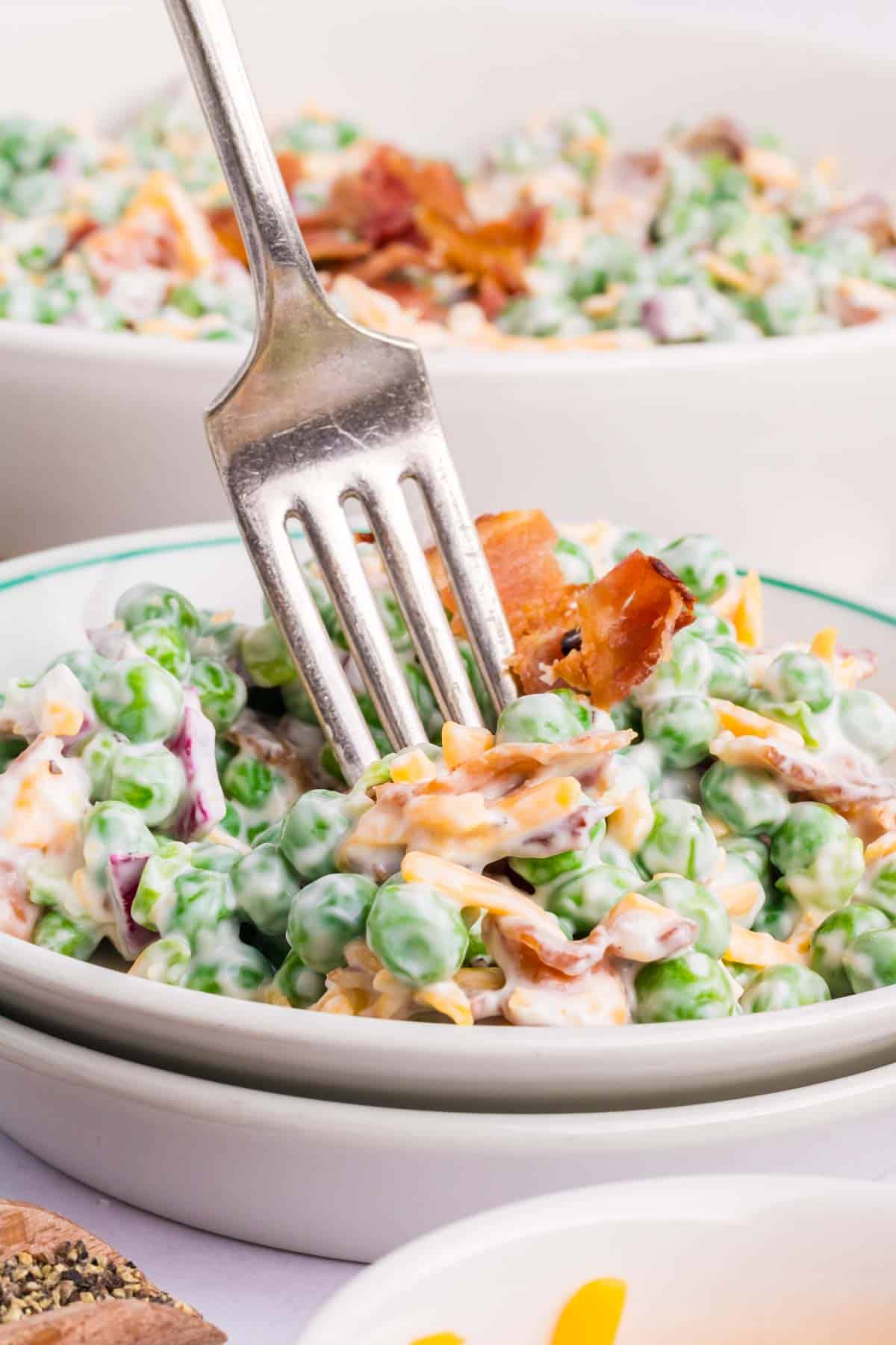 A silver fork removing a bite of green pea salad.