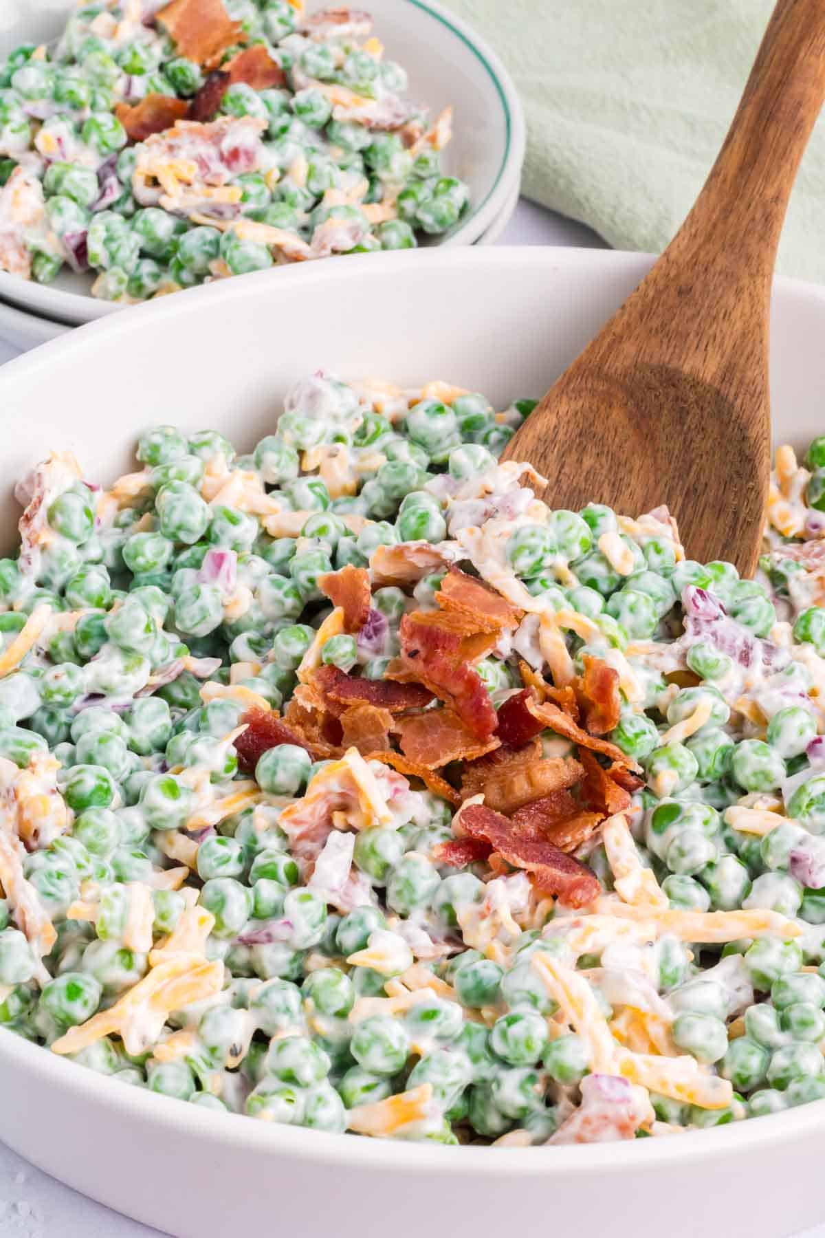 A wooden spoon serving up a scoop of green pea salad.